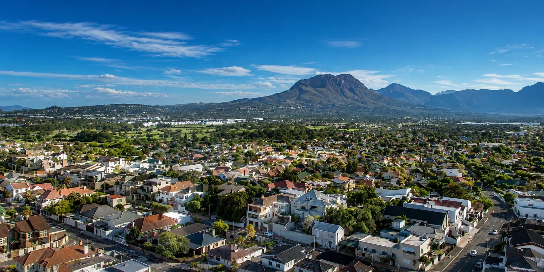 Aerial view of Somerset West and the Helderberg, with mountains in the background and tree-lined residential streets below.