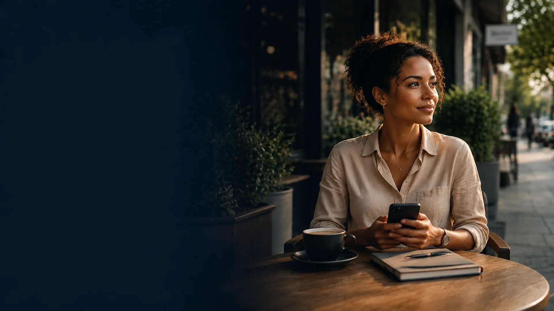 An SME business owner sitting outside a café with a coffee and notebook, looking ahead with calm confidence